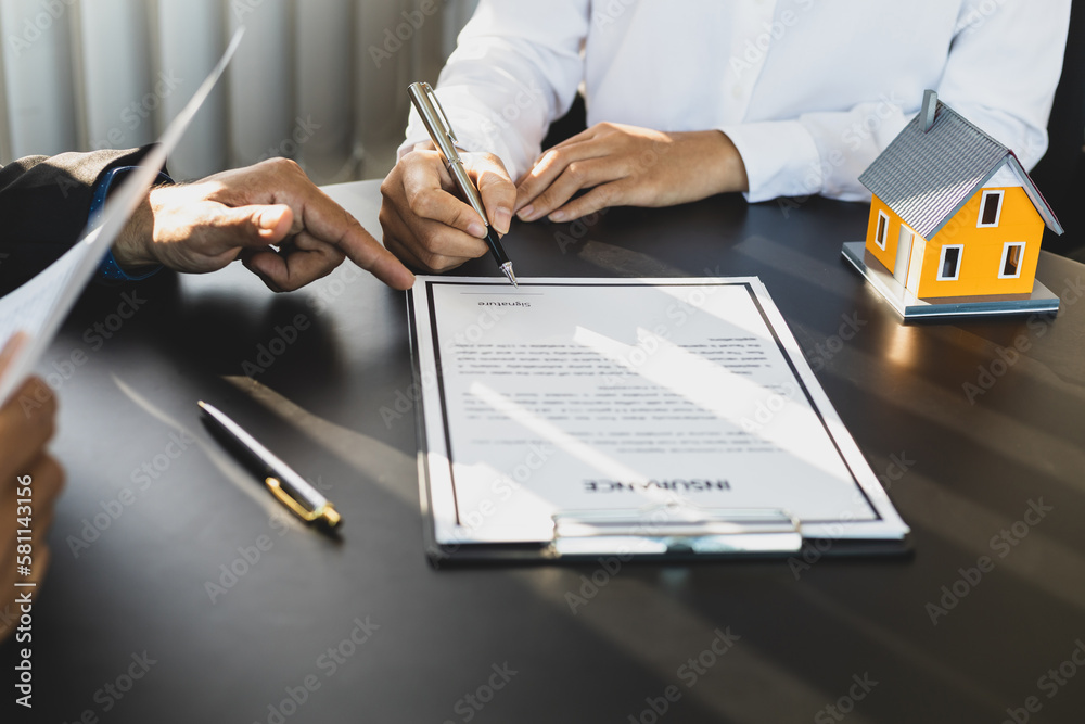 Businessman in suit in his office showing home insurance policy and pointing with a pen where the po