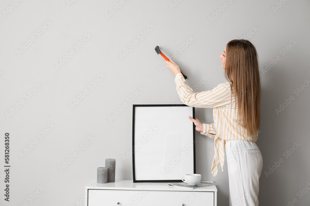 Young woman hanging blank frame on grey wall at home