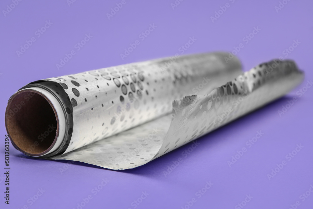 Roll of aluminium foil on lilac background, closeup