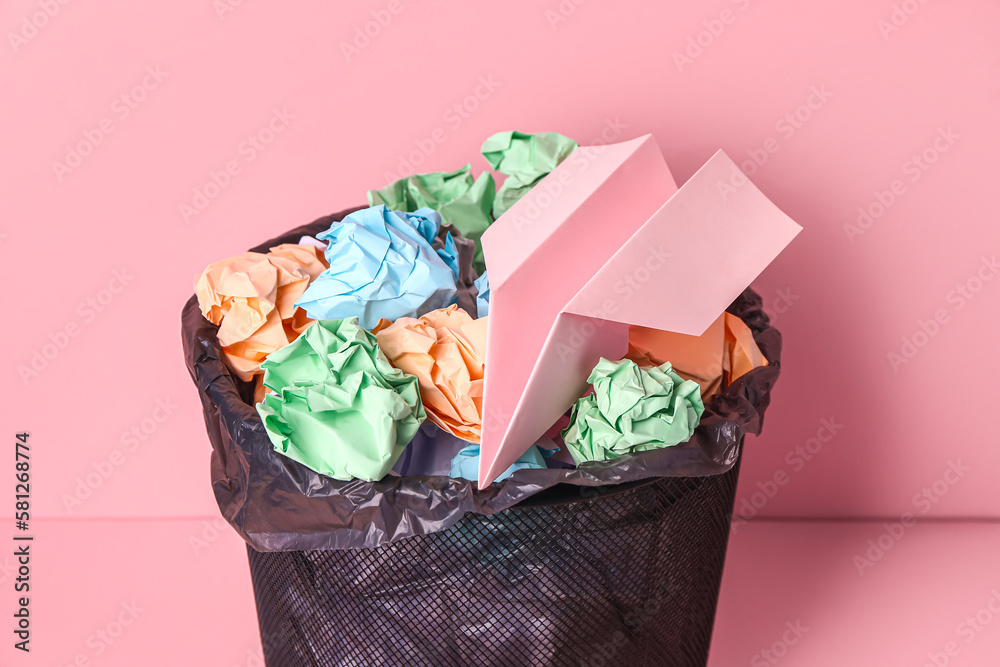 Rubbish bin with crumpled paper on pink background