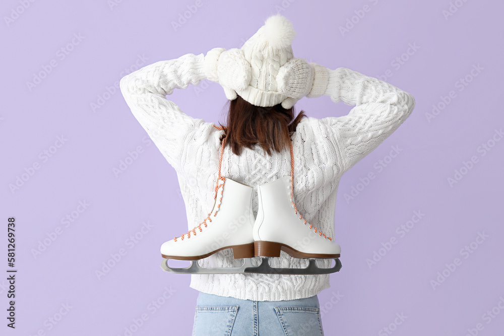 Pretty young woman with ice skates on lilac background, back view