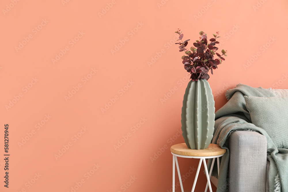 Vase with eucalyptus on table and grey sofa near pink wall