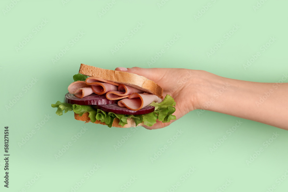 Female hand holding delicious ham sandwich on green background