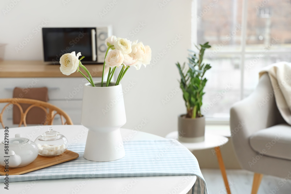 Vase with ranunculus flowers on dining table in kitchen