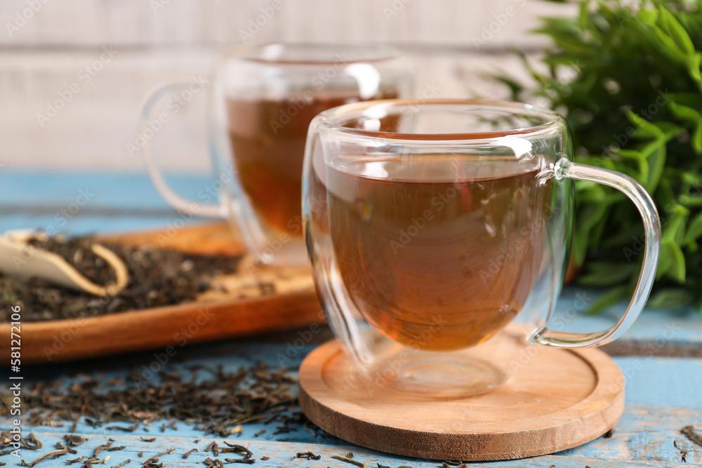 Cups of tasty green tea and dry leaves on color wooden table, closeup