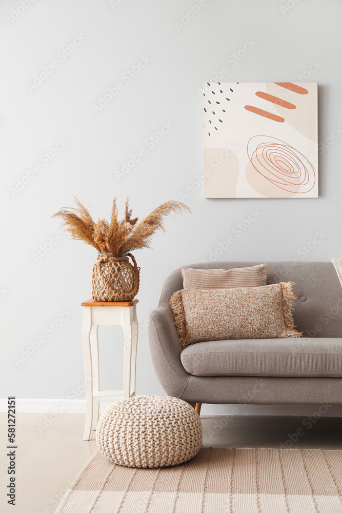 Interior of light living room with grey couch, table and pouf