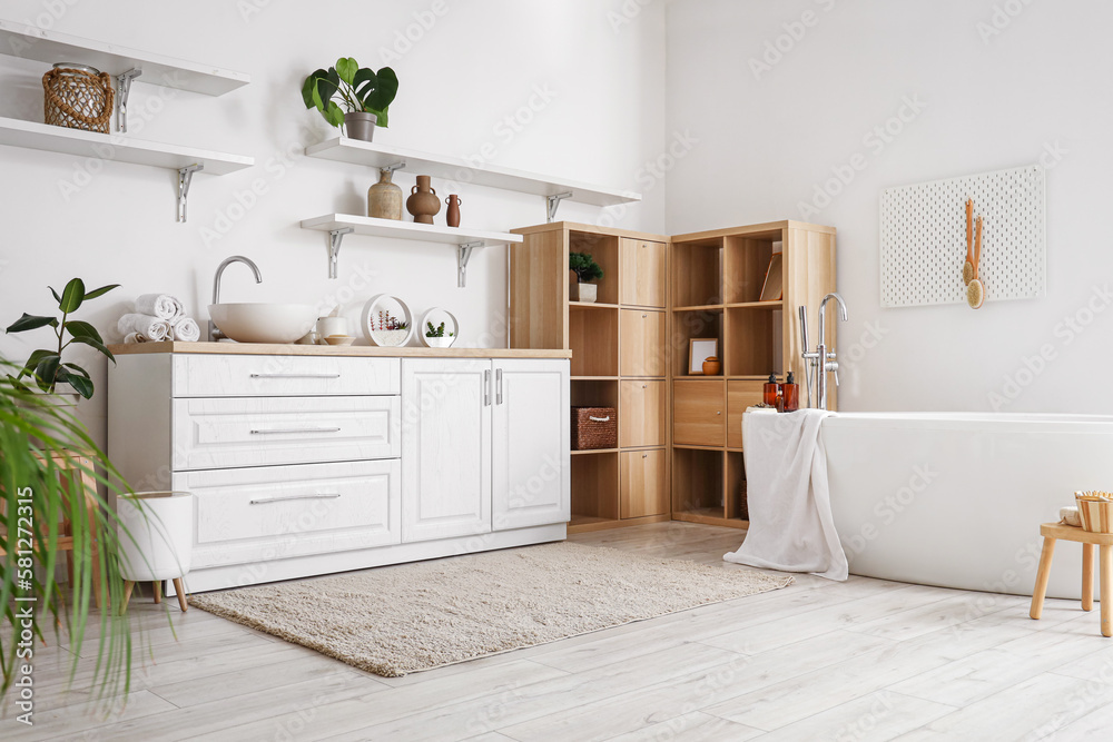 Interior of light bathroom with bathtub, counters and shelves