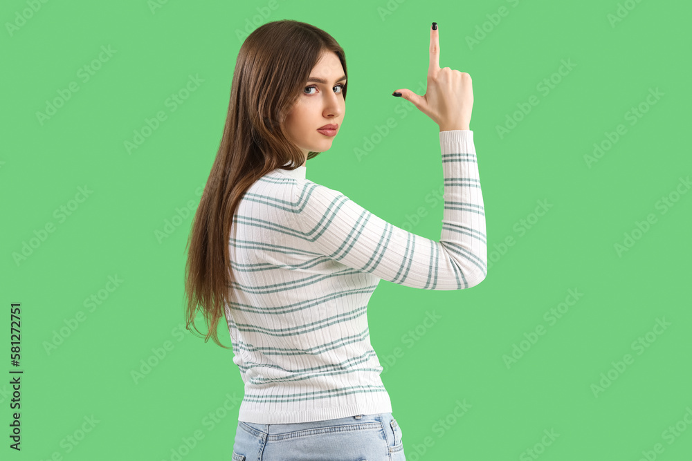 Young woman showing loser gesture on green background