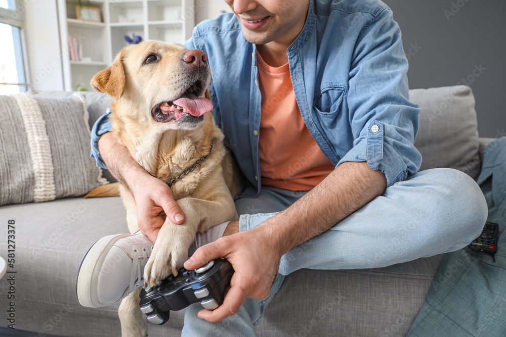 Young man with cute Labrador dog playing video game at home, closeup