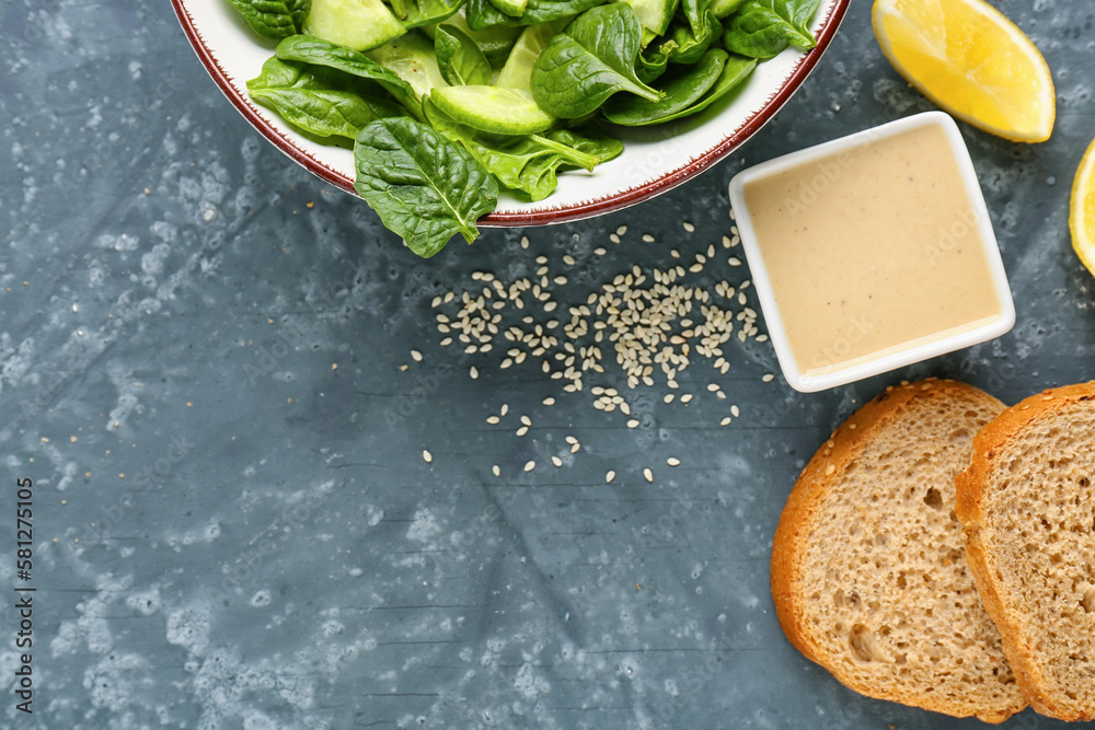 Bowl of tasty salad, tahini, bread and lemon slices on dark background