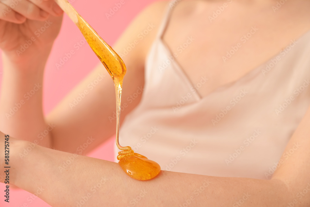 Young woman applying sugaring paste onto her arm against pink background, closeup