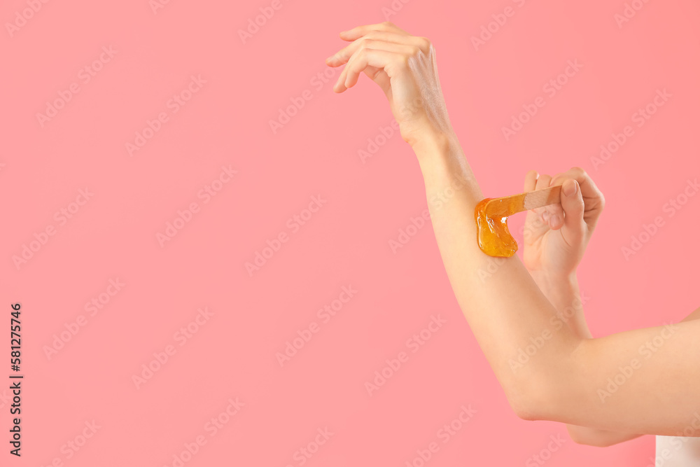 Young woman applying sugaring paste onto her arm against pink background