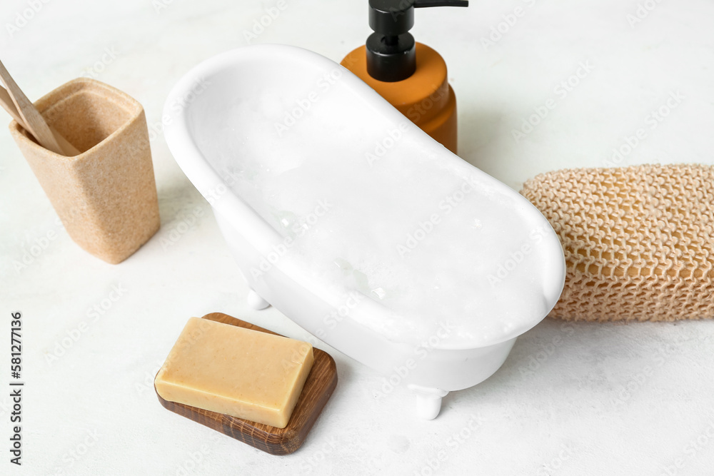 Small bathtub with foam, sponge, soap and toothbrushes on light background