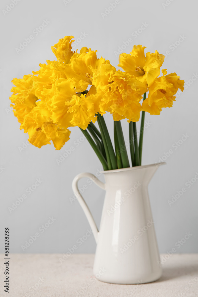 Vase with narcissus flowers on table near grey wall