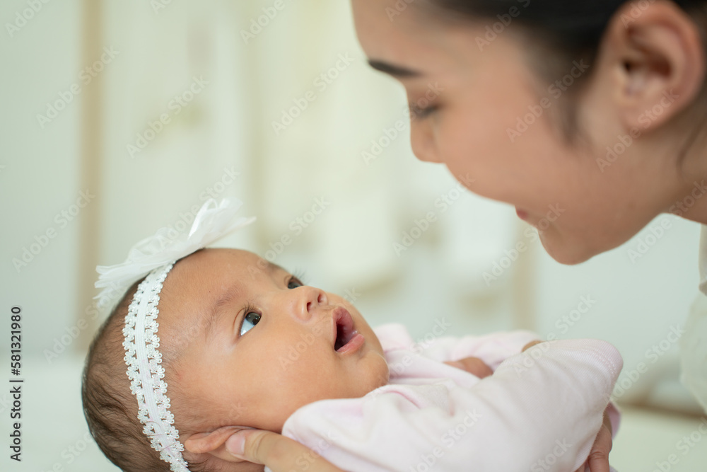 Loving Asian Mom carying of her newborn baby at home in the bedroom. happy family. mother playing wi