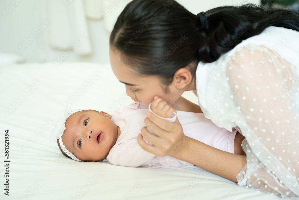 Loving Asian Mom carying of her newborn baby at home in the bedroom. happy family. mother playing wi