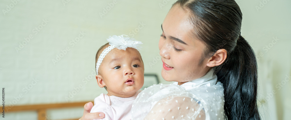 Loving Asian Mom carying of her newborn baby at home in the bedroom. happy family. mother playing wi