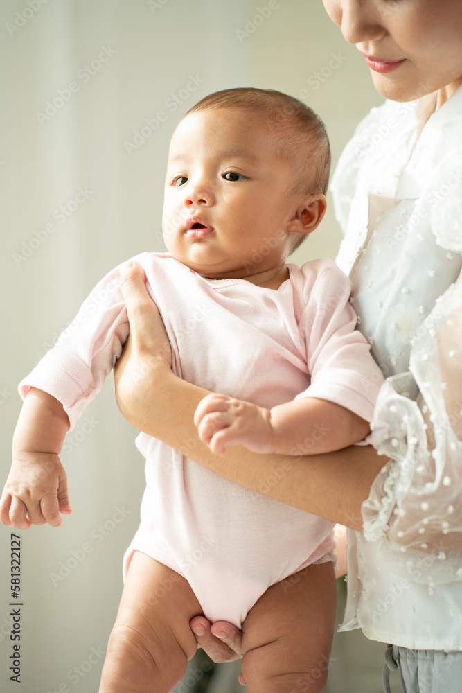 Loving Asian Mom carying of her newborn baby at home in the bedroom. happy family. mother playing wi