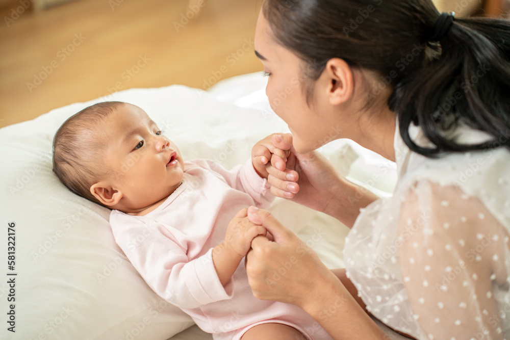 Loving Asian Mom carying of her newborn baby at home in the bedroom. happy family. mother playing wi