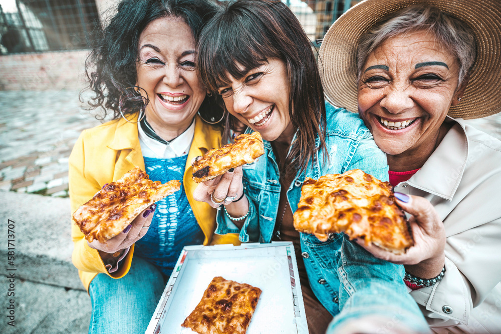 Three senior women eating pizza slice sitting outside - Happy female friends  taking selfie picture 