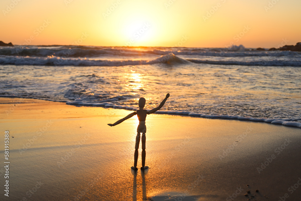 Wooden mannequin on sand near sea at sunset