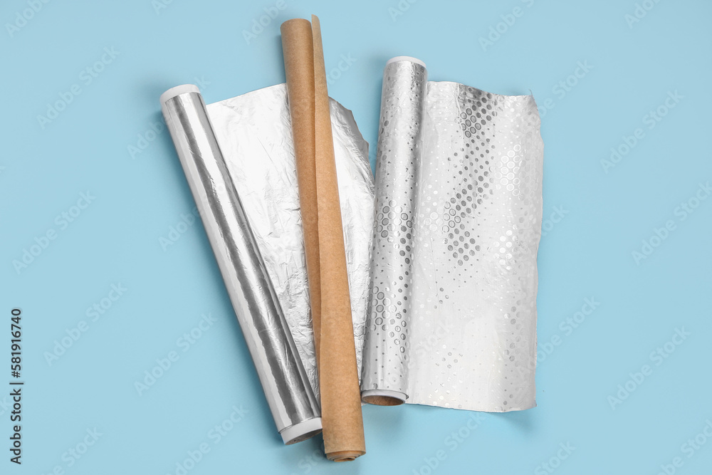 Rolls of aluminium foil and baking paper on color background