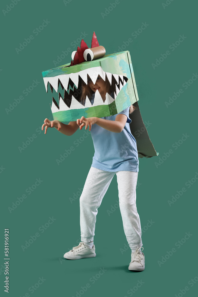 Little girl in cardboard dinosaur costume on green background