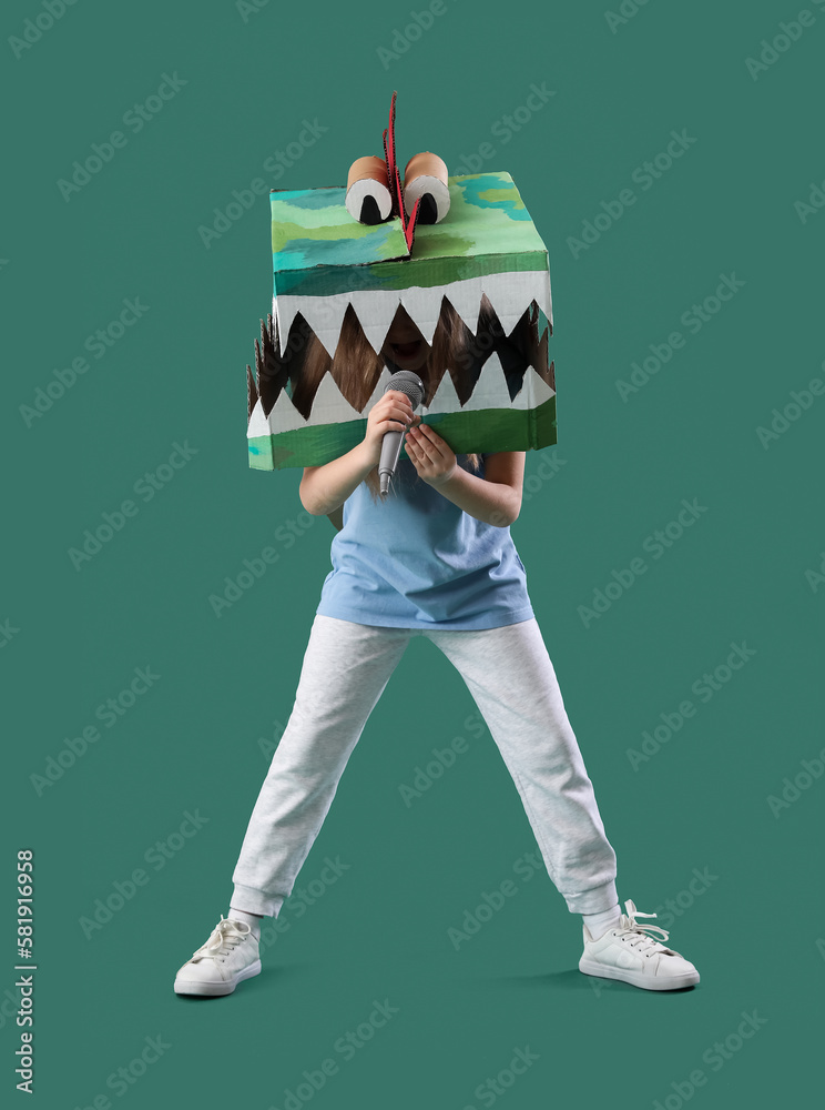 Little girl in cardboard dinosaur costume with microphone on green background