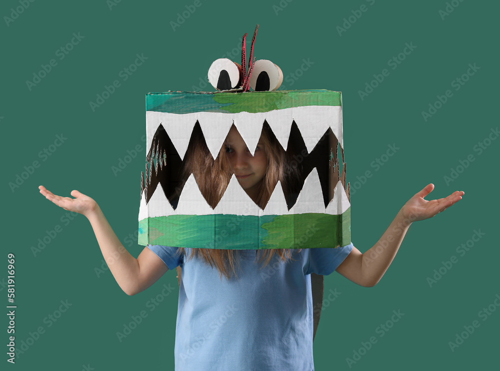 Little girl in cardboard dinosaur costume on green background