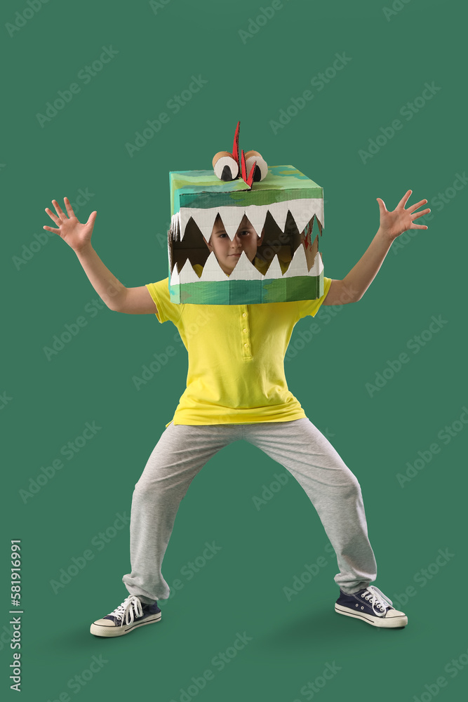 Little boy in cardboard dinosaur costume on green background