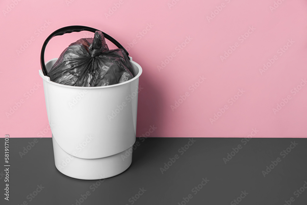 Rubbish bin with garbage bag near pink wall