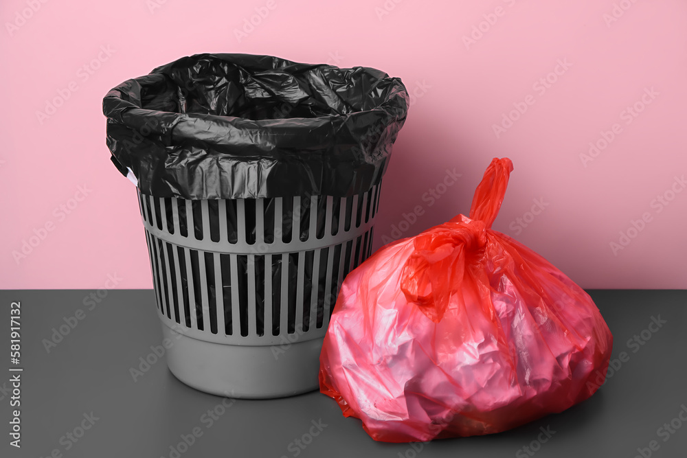 Rubbish bin and bag with garbage near pink wall