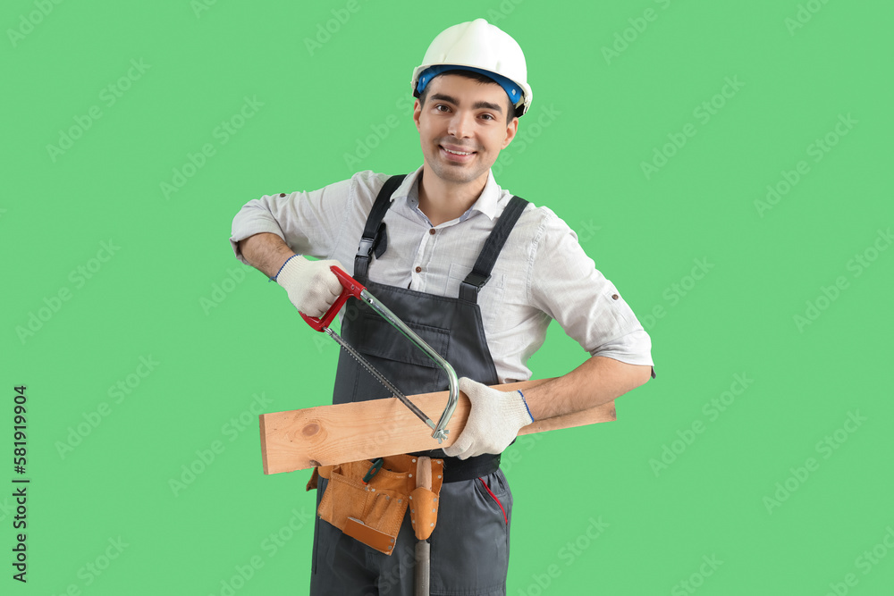 Young carpenter with hacksaw and wooden plank on green background