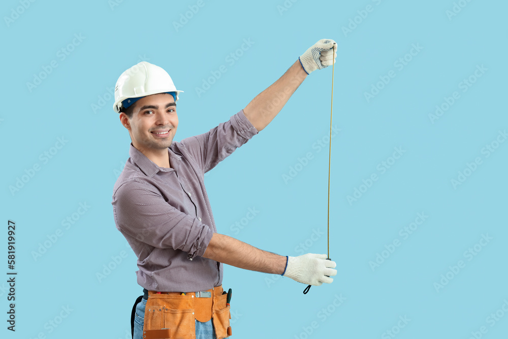 Young carpenter with tape measure on blue background