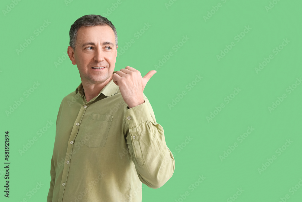 Mature man in shirt pointing at something on green background