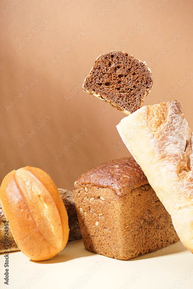 Loaves of different bread on beige table near brown wall