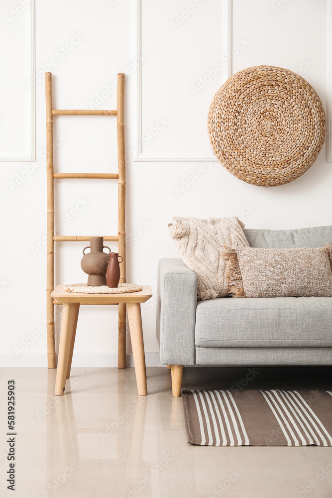 Interior of light living room with grey couch, table and ladder