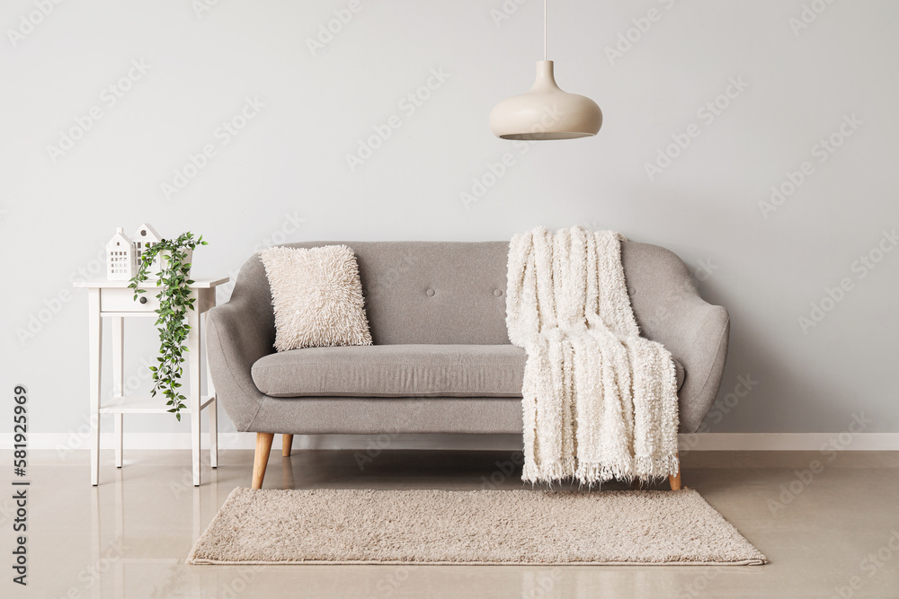 Interior of light living room with grey couch, table and lamp