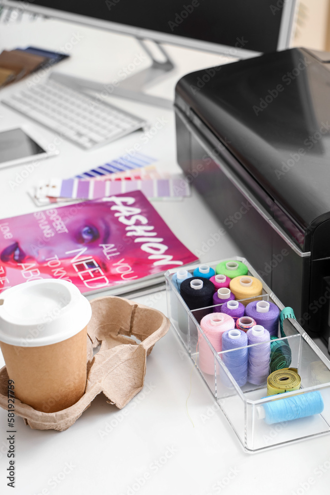 Organizer with thread spools and cup of coffee on table in atelier, closeup