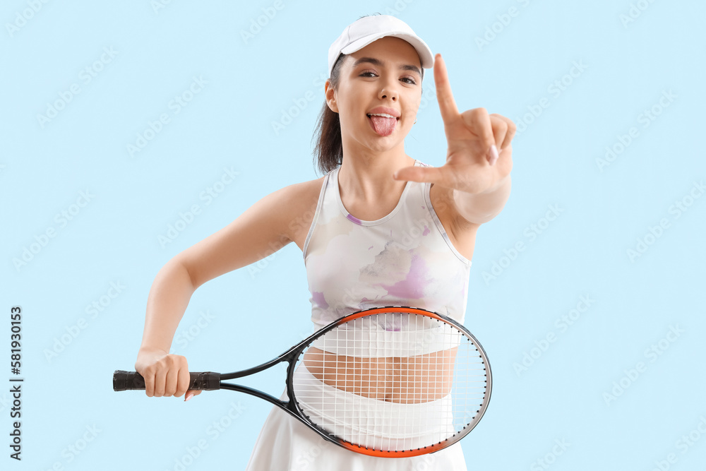 Sporty young woman with racket showing loser gesture on blue background