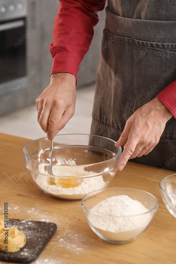 Man making dough for pasta at table in kitchen, closeup