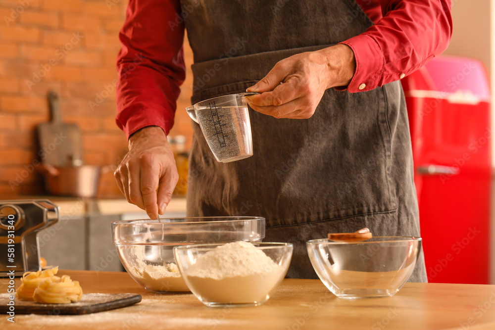 Man making dough for pasta at table in kitchen, closeup