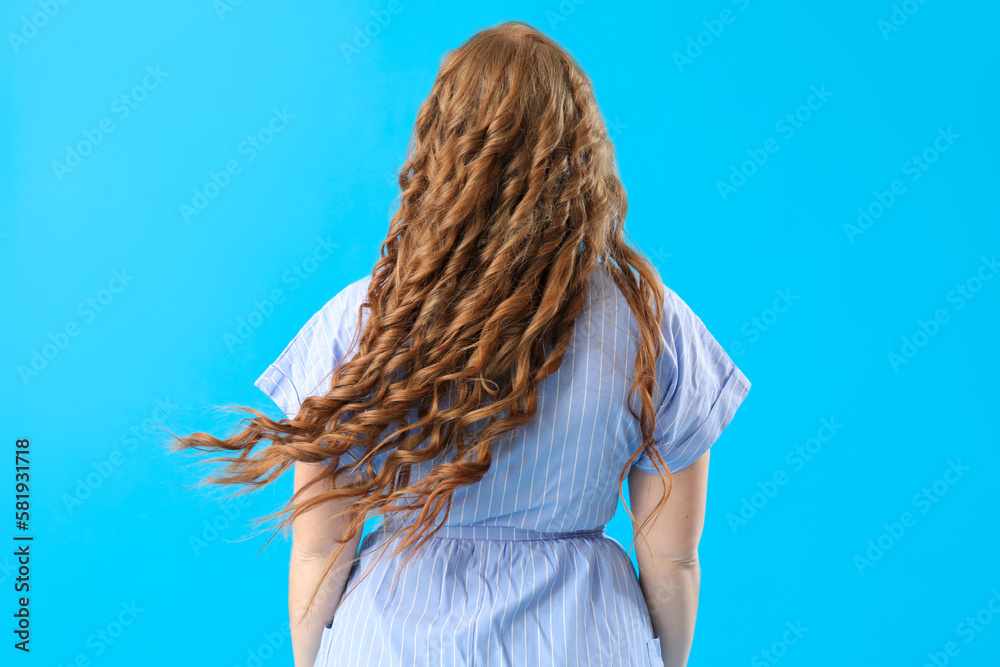 Beautiful woman with red hair on blue background, back view