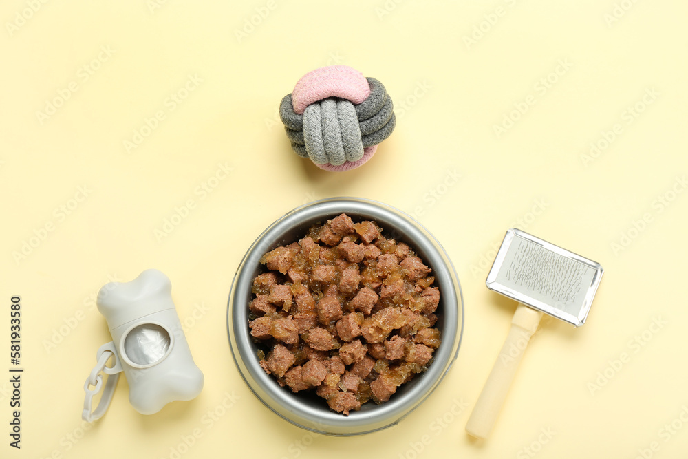 Bowl of wet pet food, grooming brush, ball and waste bags on color background