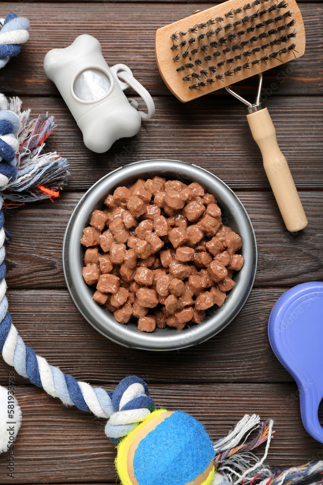 Composition with bowl of wet food and pet care accessories on wooden background