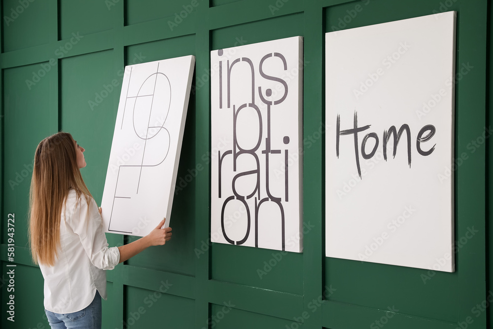 Young woman hanging poster on green wall