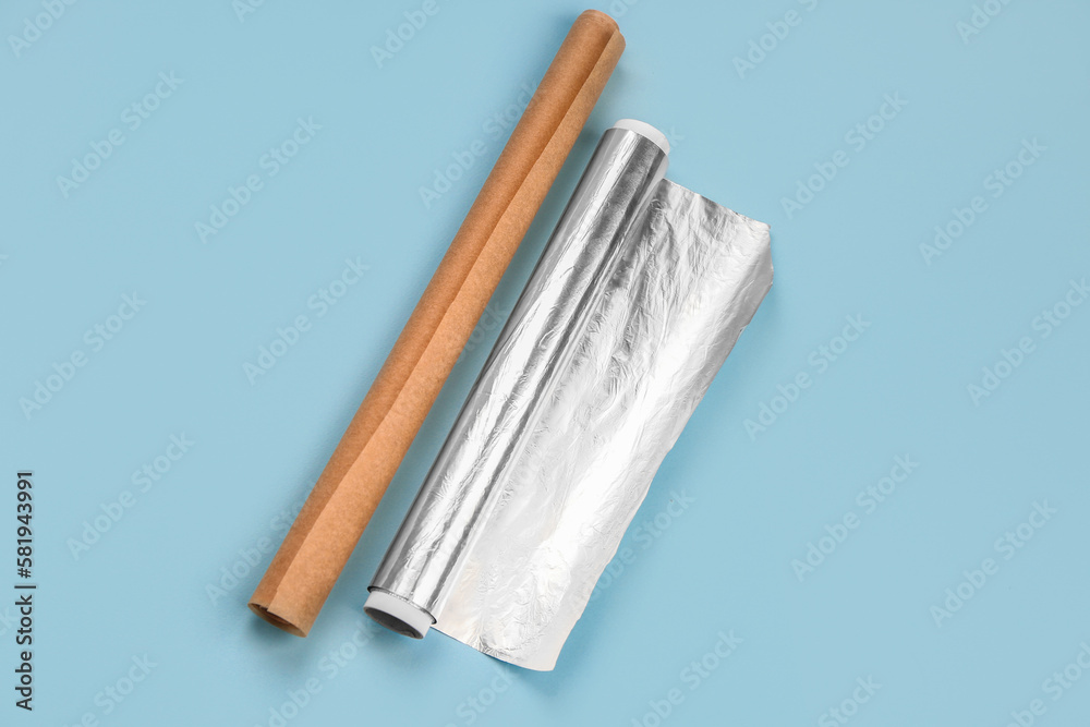 Rolls of aluminium foil and baking paper on blue background