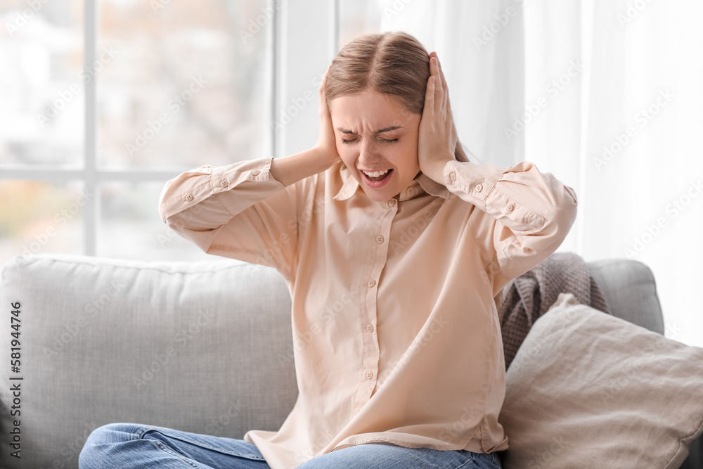 Angry young woman suffering from loud noise at home