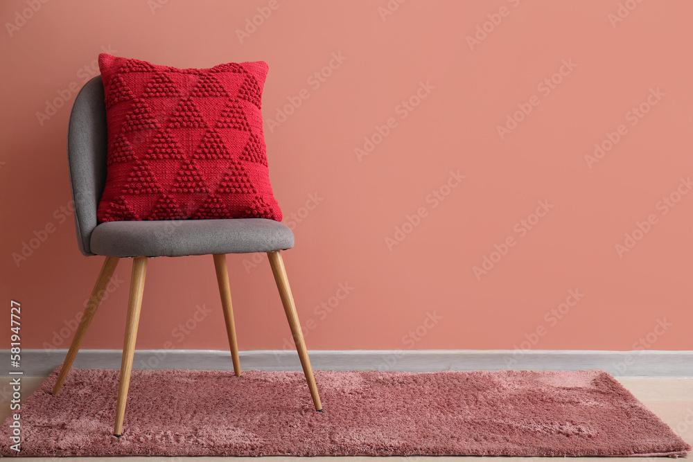 Stylish decorative pillow on grey armchair near pink wall