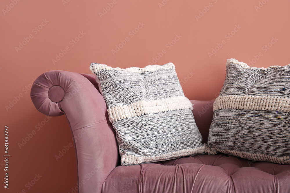 Stylish decorative pillows on cozy armchair near pink wall